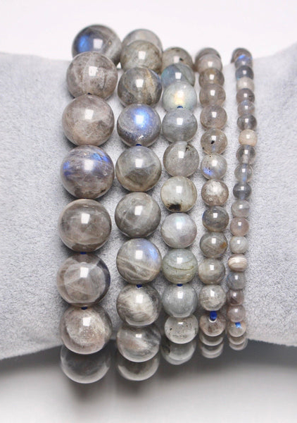 Le bracelet Opaline, composé de perles de labradorite empilées aux reflets métalliques, présentées sur un coussin gris clair sur fond blanc, évoque la sensibilité mode élégante de Mode Grande Taille. Mode Grande taille