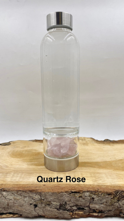 La bouteille en verre quartz rose présente un verre transparent avec des couvercles argentés et des cristaux de quartz rose au fond, idéale pour ceux qui apprécient l'élégance de la Mode Grande Taille, le tout joliment présenté sur une surface en bois. Mode Grande taille