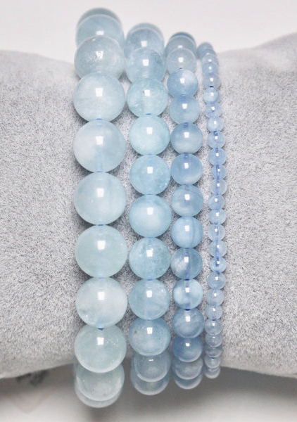 Cinq pièces du Bracelet apatite bleue, composées de perles bleu clair de différentes tailles, élégamment présentées sur un coussin gris, offrent une touche de sophistication Mode Grande Taille. Mode Grande taille