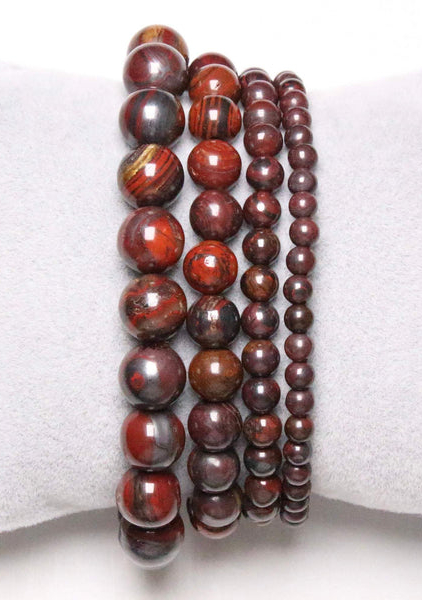 Bracelets de perles rouges et marron de différentes tailles, parfaits pour celles qui recherchent la Mode Grande Taille, présentés sur un coussin gris clair à côté de l'élégant quartz rose Bouteille en verre. Mode Grande taille