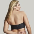 Femme aux cheveux longs blonds portant le Soutien-gorge bandeau Dana noir, regardant par-dessus son épaule, avec un fond gris clair. Mode Grande Taille. Mode Grande taille