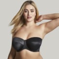 Une femme en Soutien gorge bandeau Dana noir de Mode Grande Taille pose avec une main derrière la tête sur un fond uni. Mode Grande taille