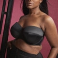 Femme en Soutien gorge bandeau Dana noir et pantalon noir, dégageant confiance sur fond rouge, mettant en valeur Mode Grande Taille. Mode Grande taille