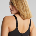 Une femme aux cheveux blonds mi-longs portant un soutien-gorge noir, légèrement tournée sur le côté pour mettre en valeur l'arrière de son Soutien-gorge balconnet Esmé Ziggy. Mode Grande taille