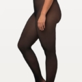 Personne portant des Collants épais aspect transparent d'Ulla Popken et un haut court noir, debout de profil sur un fond uni, mettant en valeur l'élégance de Mode Grande Taille. Mode Grande taille