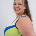 Une femme souriante dans un maillot de bain vibrant et multicolore pose sur un fond uni. Mode Grande taille