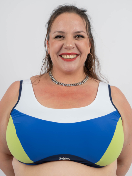 Femme souriante portant un maillot de bain bleu et blanc avec un collier ras du cou, debout devant un fond uni. Mode Grande taille