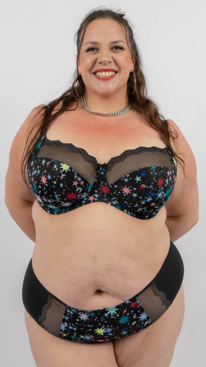 Une femme souriante en lingerie à motifs étoilés pose sur un fond blanc uni. Mode Grande taille