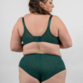 Une femme en sous-vêtements verts se tient dos à la caméra, affichant le dos d'un soutien-gorge et d'une culotte taille haute. Mode Grande taille