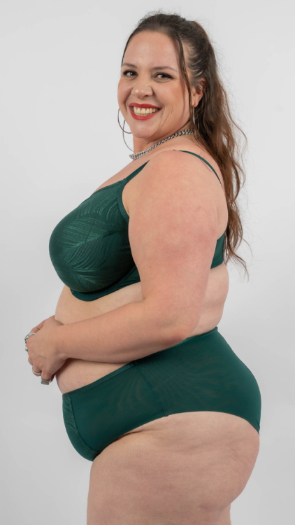 Femme souriante en lingerie verte posant sur un fond uni. Mode Grande taille