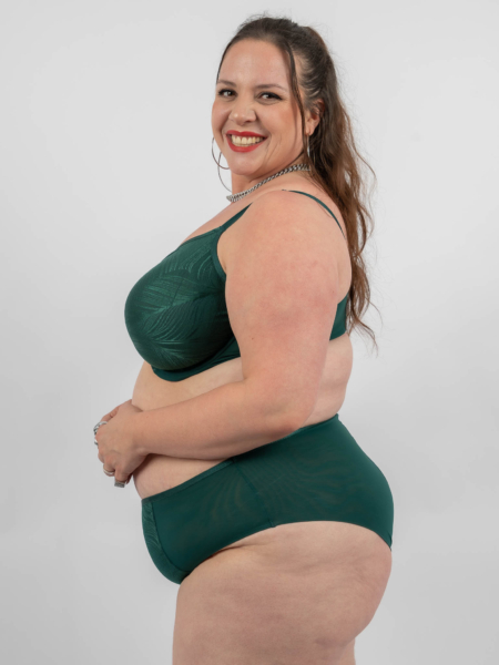 Femme souriante en lingerie verte posant sur un fond uni. Mode Grande taille