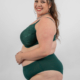 Femme souriante en lingerie verte posant sur un fond uni. Mode Grande taille