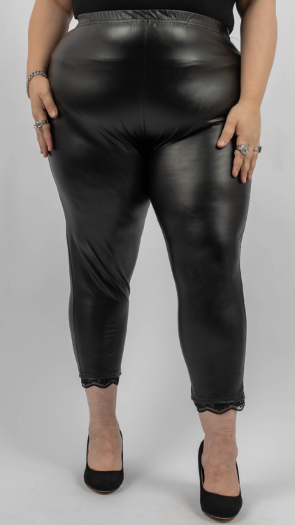 Personne portant des leggings en similicuir noir avec bordure en dentelle aux chevilles et des talons hauts noirs, debout sur un fond uni. Mode Grande taille