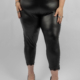 Personne portant des leggings en similicuir noir avec bordure en dentelle aux chevilles et des talons hauts noirs, debout sur un fond uni. Mode Grande taille