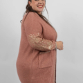 Femme souriante dans un cardigan rose avec des détails dorés sur les manches, posant sur un fond blanc uni. Mode Grande taille