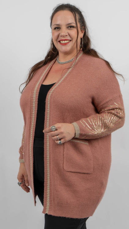 Femme souriante dans un cardigan rose avec des accents métalliques et un haut noir, posant sur un fond uni. Mode Grande taille