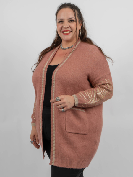 Femme souriante dans un cardigan rose avec des accents métalliques et un haut noir, posant sur un fond uni. Mode Grande taille