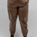 Personne portant un pantalon de jogging en cuir marron taille haute avec poches avant et chevilles élastiquées, debout sur un fond gris. Mode Grande taille