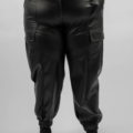 Personne portant un pantalon noir taille haute en similicuir avec une fermeture à glissière, des poches latérales et des poignets élastiques aux chevilles. Mode Grande taille