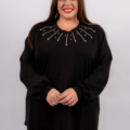 Femme souriante aux cheveux longs, portant un haut noir avec un léger motif décoratif près de l'encolure, pose sur un fond gris. Mode Grande taille