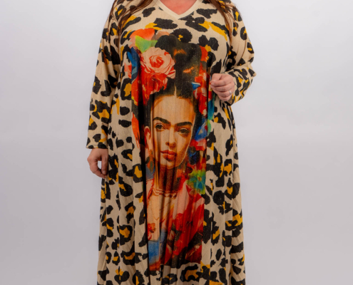 Femme portant une longue robe à imprimé léopard représentant un grand portrait de Frida Kahlo, debout et souriante sur fond blanc. Mode Grande taille