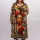 Femme portant une longue robe à imprimé léopard représentant un grand portrait de Frida Kahlo, debout et souriante sur fond blanc. Mode Grande taille