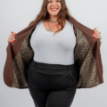 Une femme souriante ouvre son blazer marron pour révéler une doublure à imprimé léopard, portant un haut blanc et un pantalon noir. Mode Grande taille