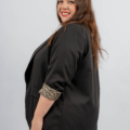 Femme aux longs cheveux bruns, portant un blazer noir avec des poignets à imprimé léopard, souriant à la caméra sur un fond blanc. Mode Grande taille