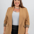 Femme aux cheveux longs portant un blazer beige avec des poignets à imprimé léopard, un haut blanc et un pantalon noir, souriant à la caméra. Mode Grande taille