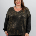 Femme souriante et portant un pull moucheté noir et or avec un pantalon noir, debout sur un fond uni. Mode Grande taille