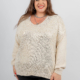 Femme souriante aux longs cheveux bruns portant un pull de couleur crème avec un motif scintillant et un pantalon noir. Mode Grande taille