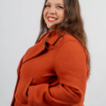 Une femme portant un manteau orange, souriante, les mains dans les poches, se tient debout sur un fond blanc uni. Mode Grande taille