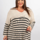 Femme souriante dans un pull rayé avec des lignes horizontales noires et blanches, debout sur un fond uni. Mode Grande taille