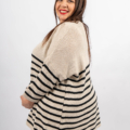 Une femme souriante portant un pull rayé beige et noir se tient debout sur un fond blanc. Mode Grande taille