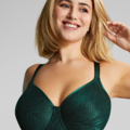 Une personne souriante aux cheveux blonds mi-longs portant le Soutien Gorge Emboîtant Illuminate en vert émeraude, posant sur un fond gris clair. Mode Grande taille