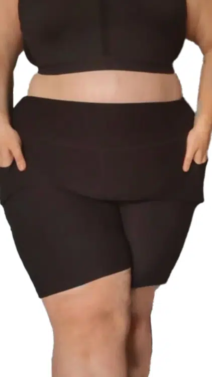 Une personne portant un soutien-gorge de sport assorti et un short à poches noir avec les mains dans les poches du short. Mode Grande taille