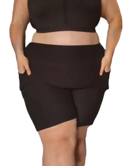 Une personne portant un soutien-gorge de sport assorti et un short à poches noir avec les mains dans les poches du short. Mode Grande taille