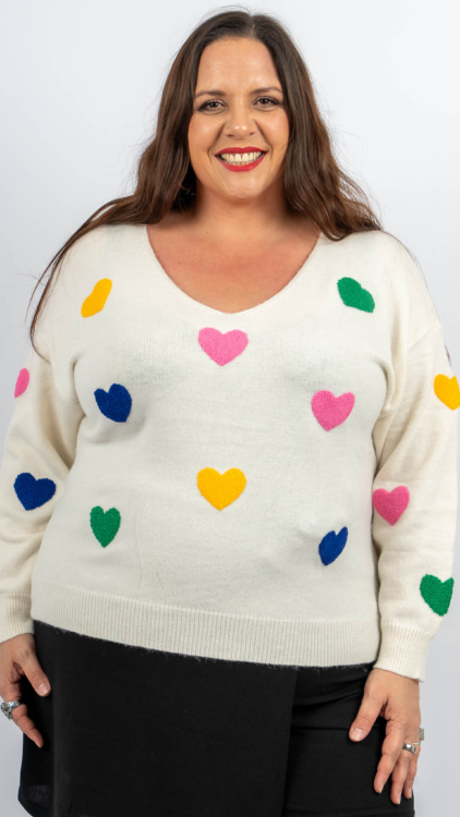 Femme souriante dans un pull blanc avec des motifs de cœurs colorés. Mode Grande taille