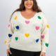 Femme souriante dans un pull blanc avec des motifs de cœurs colorés. Mode Grande taille