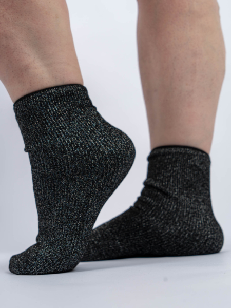 Deux pieds portant des chaussettes noires scintillantes sont représentés sur un fond uni. Mode Grande taille