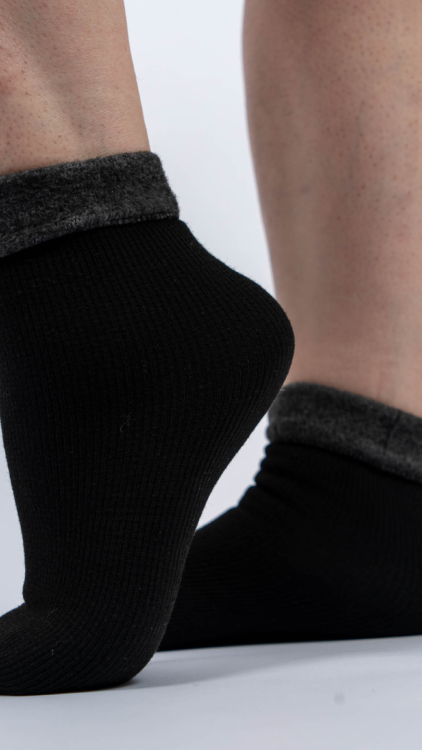 Personne portant des chaussettes noires avec des revers gris pelucheux, debout sur un fond blanc. Mode Grande taille