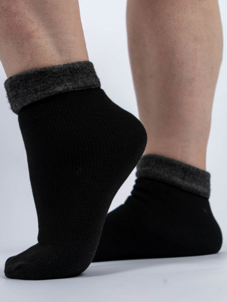 Personne portant des chaussettes noires avec des revers gris pelucheux, debout sur un fond blanc. Mode Grande taille