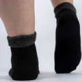 Gros plan d'une personne portant des chaussettes noires avec des revers gris, debout sur une surface gris clair. Mode Grande taille