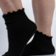 Gros plan de pieds portant des chaussettes noires à bords volantés sur fond blanc. Mode Grande taille