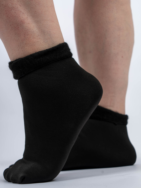 Gros plan de pieds portant des chaussettes noires à revers pelucheux, debout sur une surface claire. Mode Grande taille