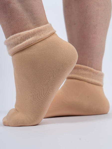 Gros plan d'une personne portant des chaussettes beiges avec un revers doux et moelleux, debout sur une surface blanche. Mode Grande taille