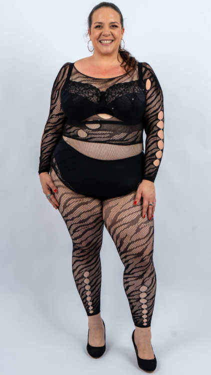 Femme souriante en tenue à motifs noirs posant sur un fond blanc uni. Mode Grande taille