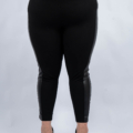 Une personne portant des leggings noirs avec des accents en cuir, debout avec des talons noirs sur un fond uni. Mode Grande taille