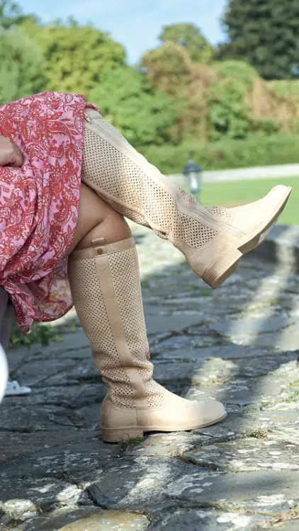 Une personne portant une robe à motifs rouges et des bottes beiges à mollet large Colette XL Gabylou est assise sur un banc dans un parc. Mode Grande taille