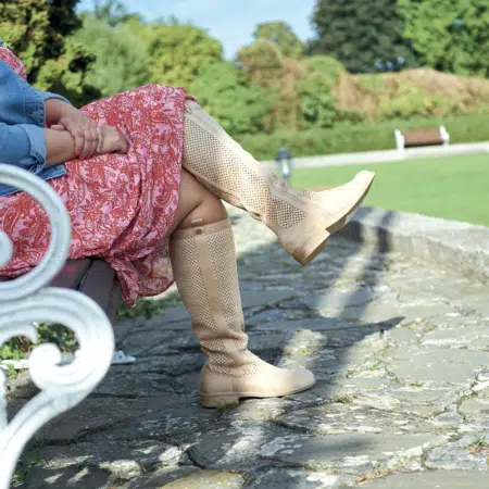 Une personne portant une robe à motifs rouges et des bottes beiges à mollet large Colette XL Gabylou est assise sur un banc dans un parc. Mode Grande taille